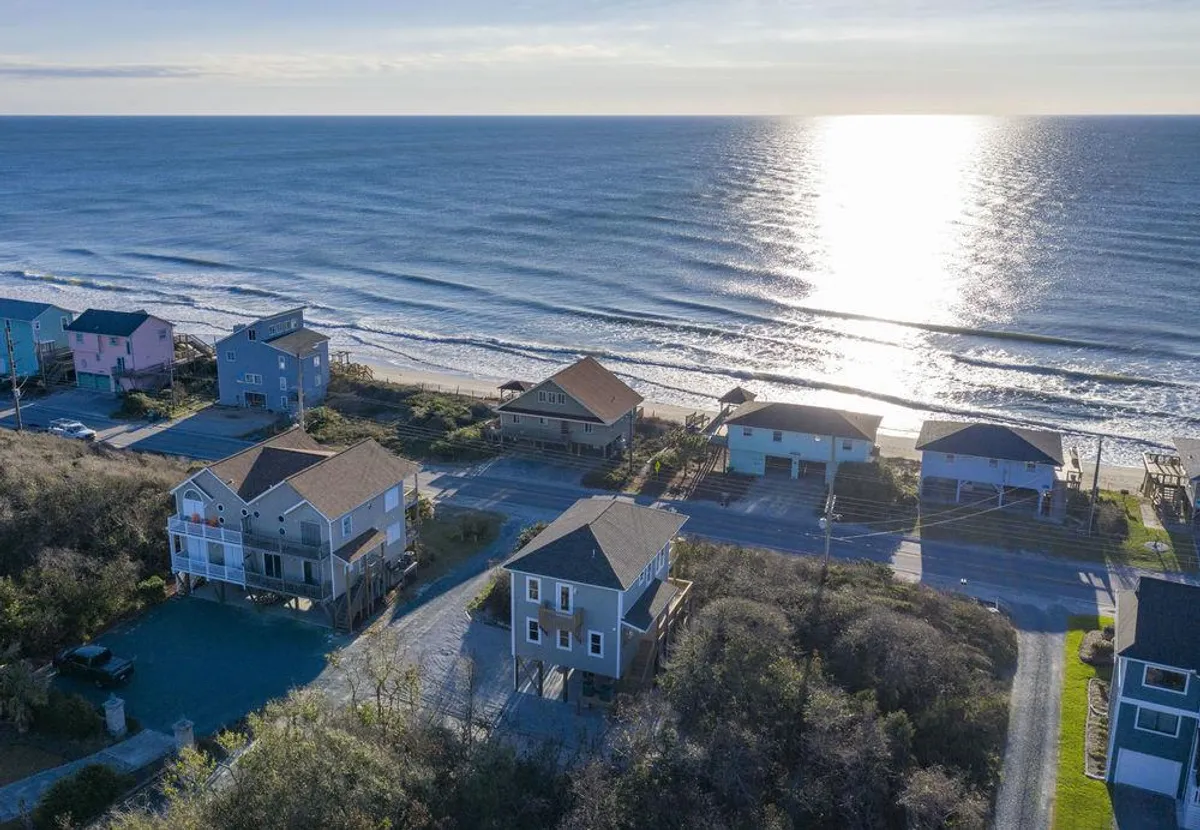 This exterior image captures a stunning stretch of ocean, beachfront houses, and a winding road. The late afternoon or evening light gives it a relaxed, inviting atmosphere, with the beach ready for exploration and social activities.