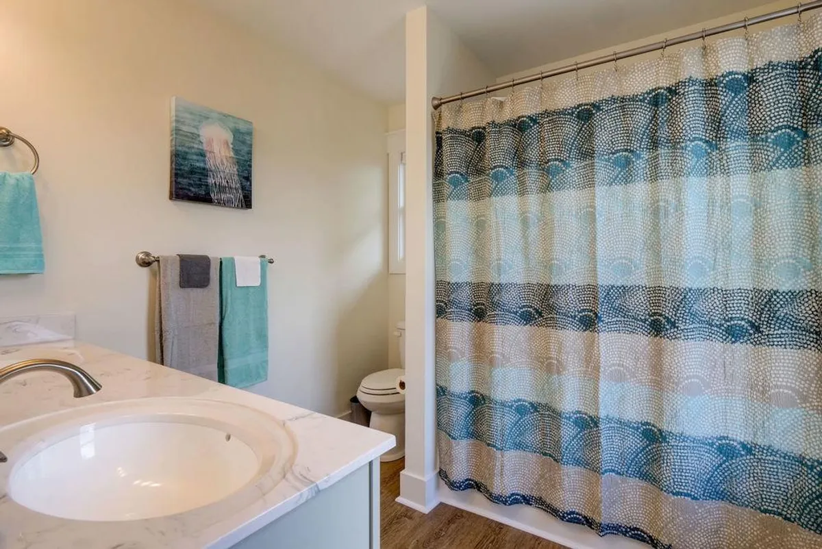 A tranquil bathroom scene featuring a vanity with sink, a colorful shower curtain, and wall art, creating an inviting space for refreshing baths and morning rituals.