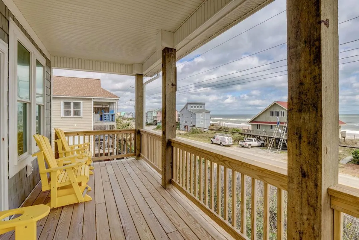 The balcony view highlights yellow Adirondack chairs arranged to face an expansive ocean vista over a wooden railing. The scene invites guests to enjoy fresh air, breathtaking sunrises or sunsets, and casual outdoor gatherings.