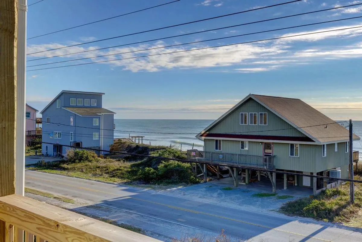 A scenic view shows beach houses lining the coast with the road leading directly toward the ocean. The expansive ocean view, with soft sand and coastal vegetation, captures the proximity of the property to the beach and the vibrant coastal community.