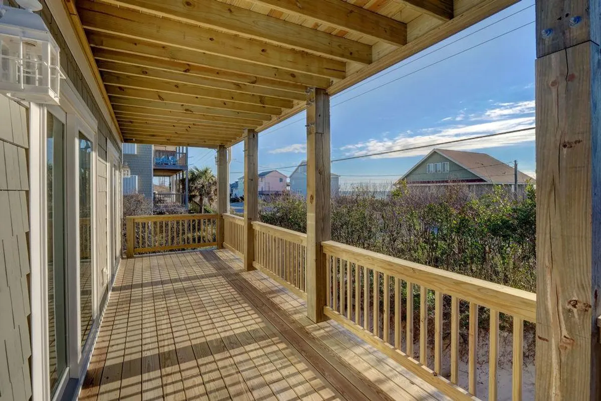 A tranquil wooden porch surrounded by greenery, with distant houses visible. The scene feels peaceful, inviting guests to relax outdoors, perhaps after a day of kayaking, fishing, or exploring nature.