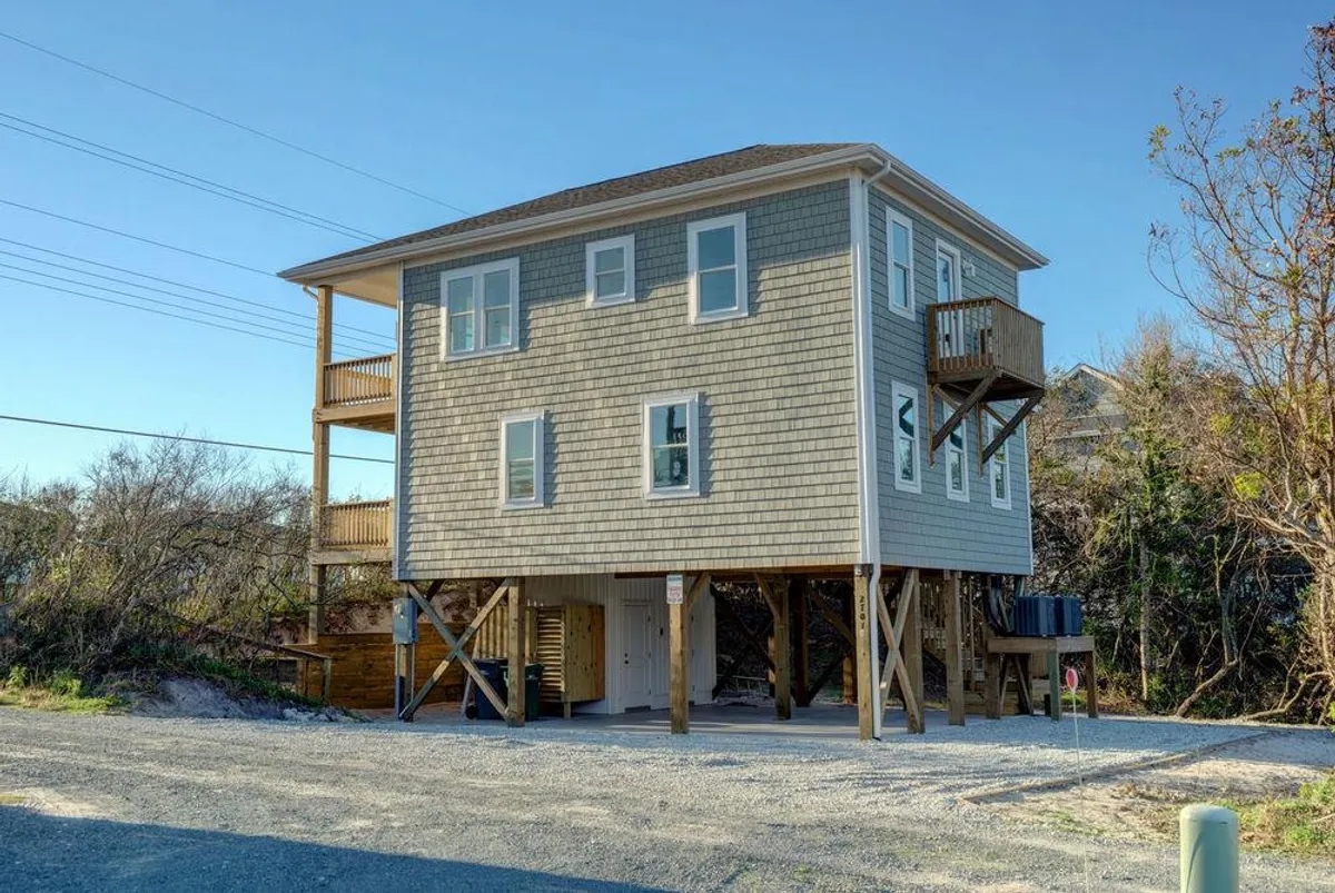 An exterior view of the property highlights its elevated structure, spacious balconies, and large windows. The scene suggests opportunities for relaxing, socializing, and enjoying sunsets from the comfort of your own private space.