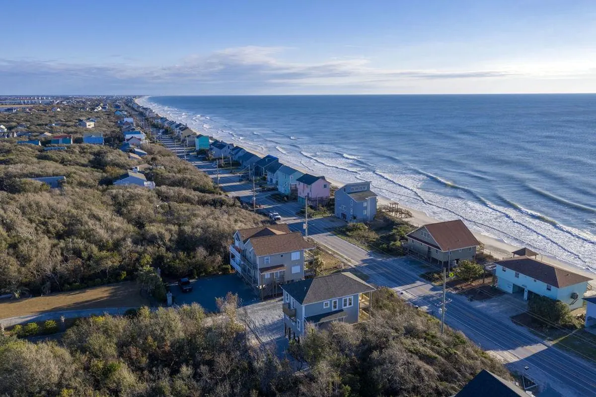 A panoramic view of ocean waves, rows of beach houses, and the main coastal road. The scene is active yet tranquil, suggesting both daytime relaxation and evening adventures along the shore and through town.